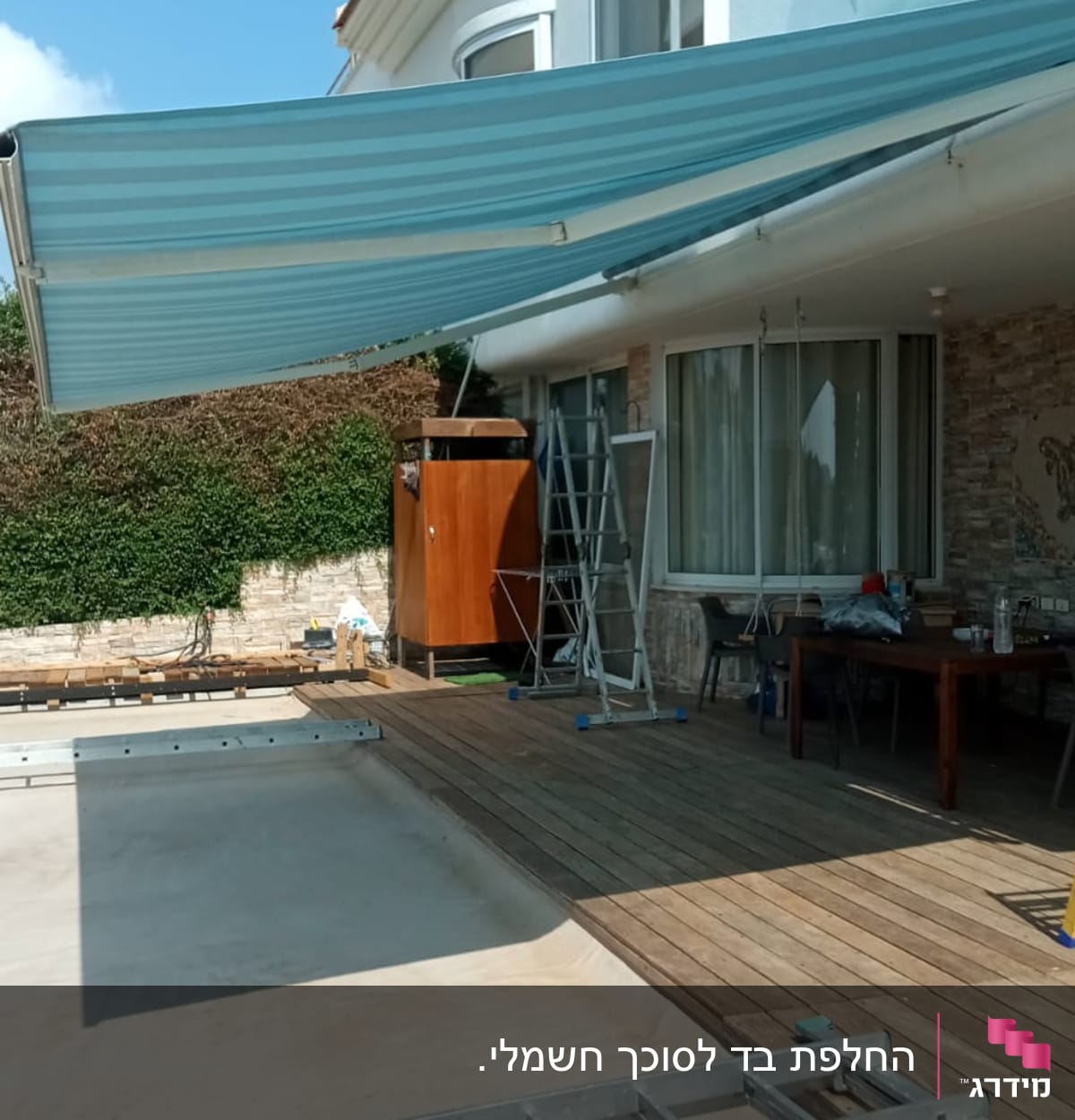 סוכך בד פסים כחול מותקן מעל מרפסת עץ